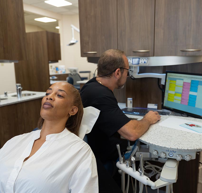 A female patient waits at the dental chair as Dr. Owen M. Waldman works on the computer behind her