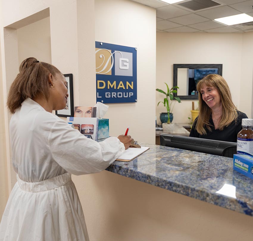 A female guest signs a paper in front of a smiling female dental staff inside the office of the Waldman Dental Group